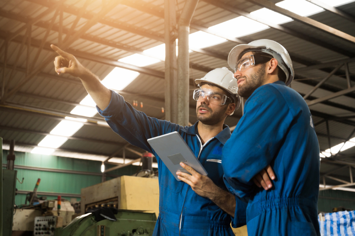 Two operators in a factory, using a tablet and pointing at something in the distance